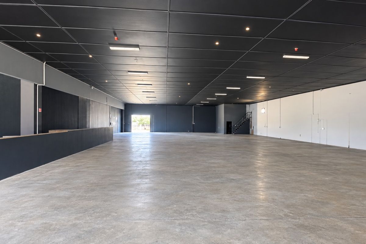 A spacious, open-plan retail or industrial unit featuring polished concrete floors, a modern dark suspended ceiling with recessed lighting, and a built-in service counter.