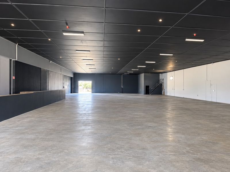 A spacious, open-plan retail or industrial unit featuring polished concrete floors, a modern dark suspended ceiling with recessed lighting, and a built-in service counter.