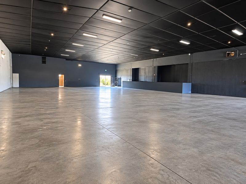 Spacious open-plan retail or commercial area featuring polished concrete flooring, a modern dark suspended ceiling with recessed lighting, and a built-in service counter.
