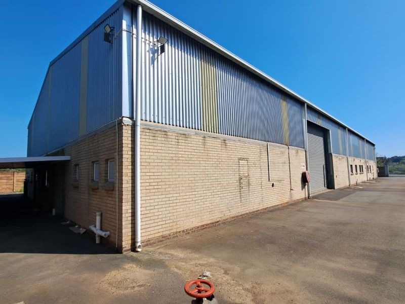Rear view of an industrial warehouse featuring corrugated metal cladding, face brick walls, and a roller shutter door with an adjacent asphalt yard.