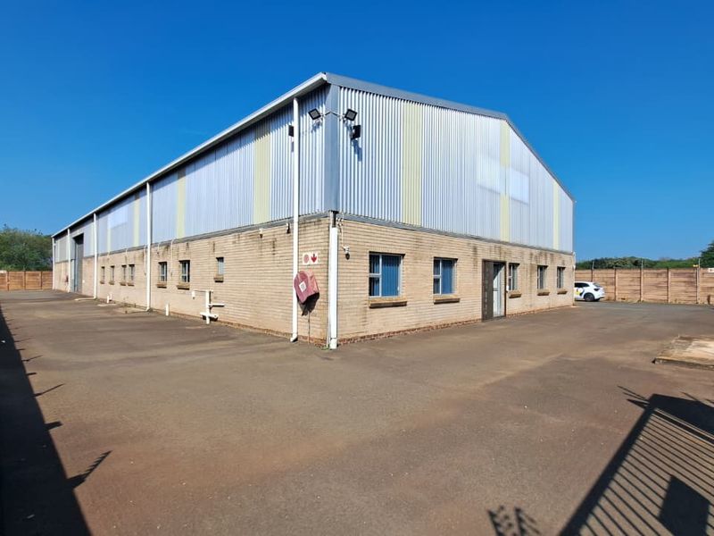 Industrial warehouse building featuring a combination of face brick and corrugated metal cladding, set within a secure perimeter with an expansive asphalt yard.