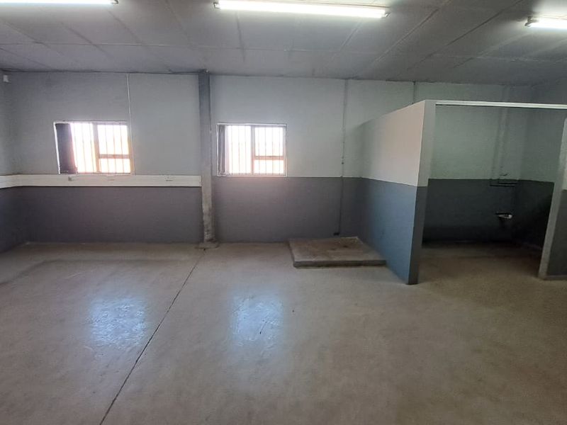 An empty industrial office space featuring concrete floors, fluorescent lighting, and security-barred windows, offering a functional blank canvas for business operations.