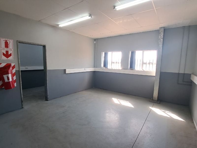 A clean, functional industrial utility space featuring concrete flooring, secure window bars, and overhead fluorescent lighting, suitable for office or storage use.