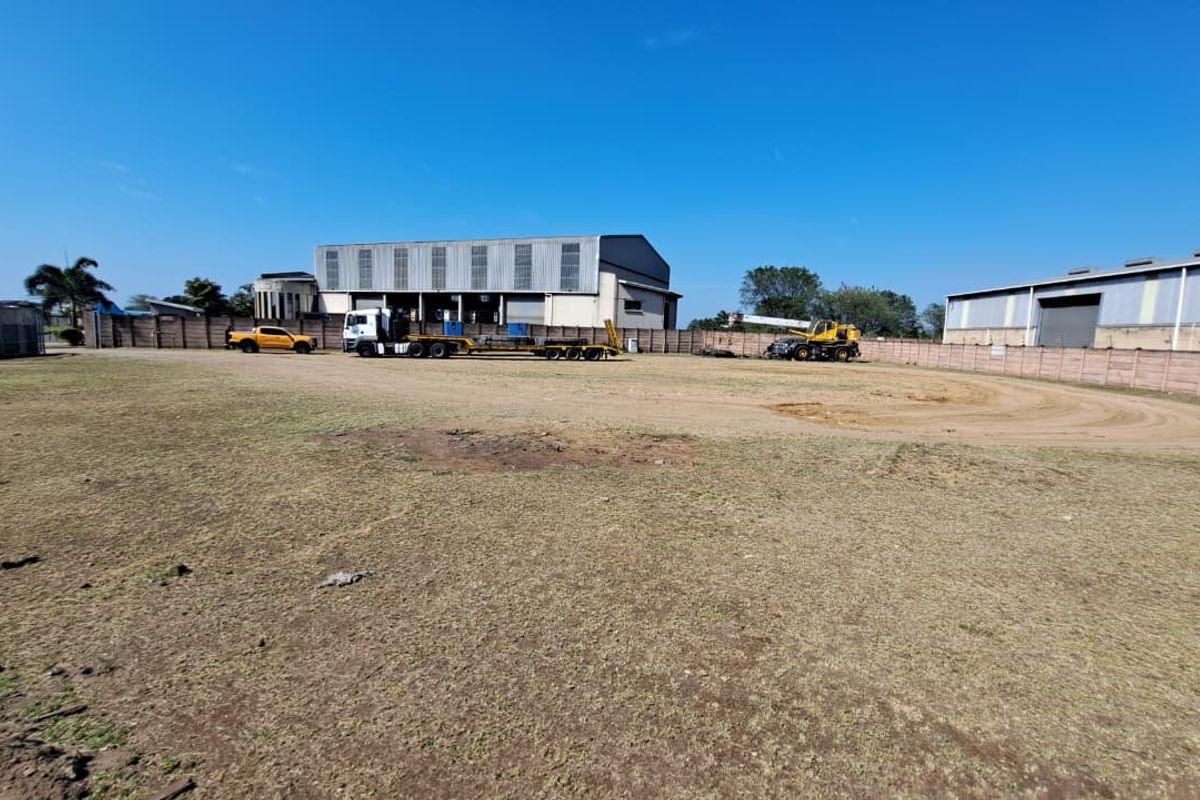 A wide-angle view of an industrial property featuring a large open yard area enclosed by a perimeter wall with warehouse buildings in the background.