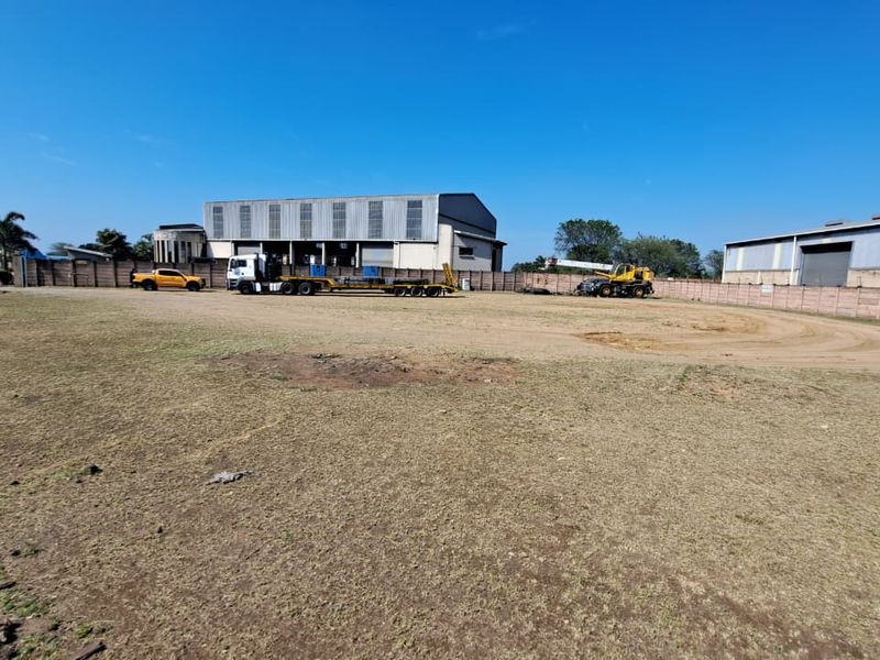 A wide-angle view of an industrial property featuring a large open yard area enclosed by a perimeter wall with warehouse buildings in the background.