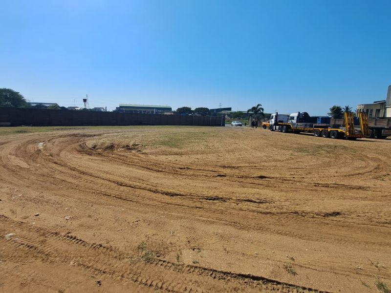 Large open industrial yard space with perimeter walling and adjacent warehouse structure, suitable for heavy vehicle access or storage.