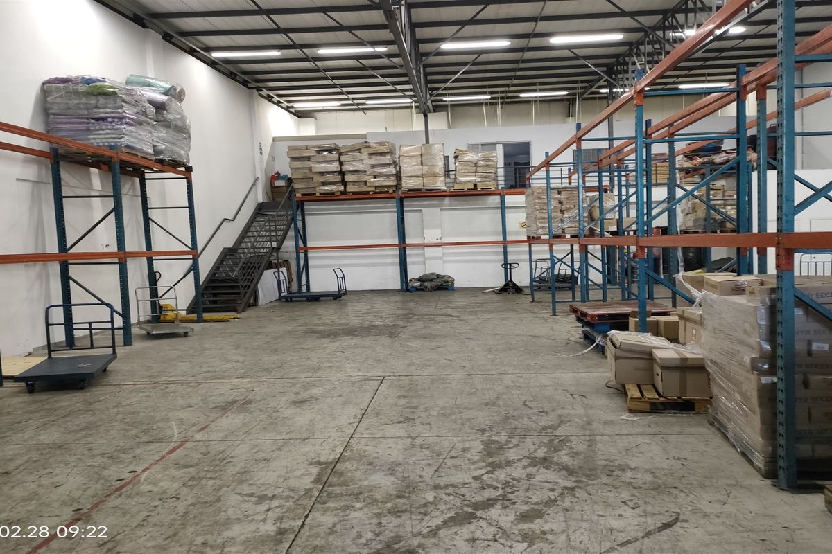 Spacious industrial warehouse featuring high ceilings, exposed steel roof trusses, and extensive built-in metal racking systems for efficient storage and logistics.