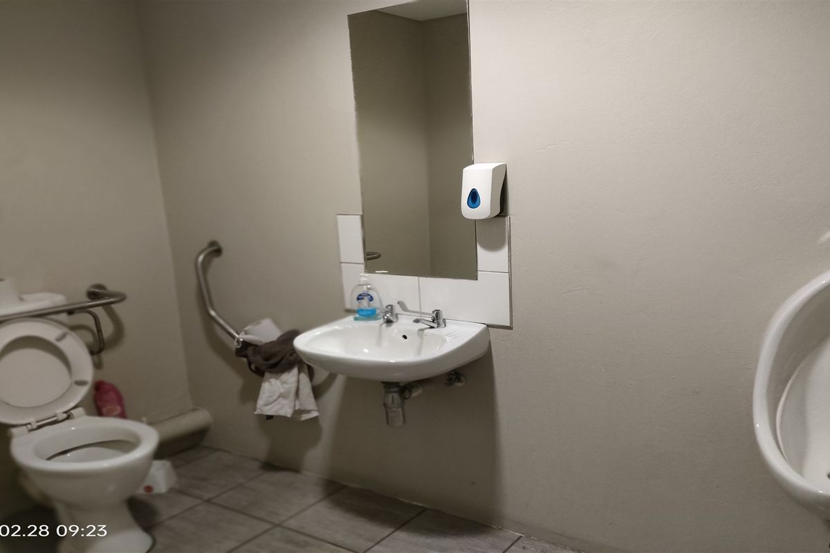 Functional industrial restroom featuring a wall-mounted basin, toilet with grab rails, and a wall-mounted urinal.