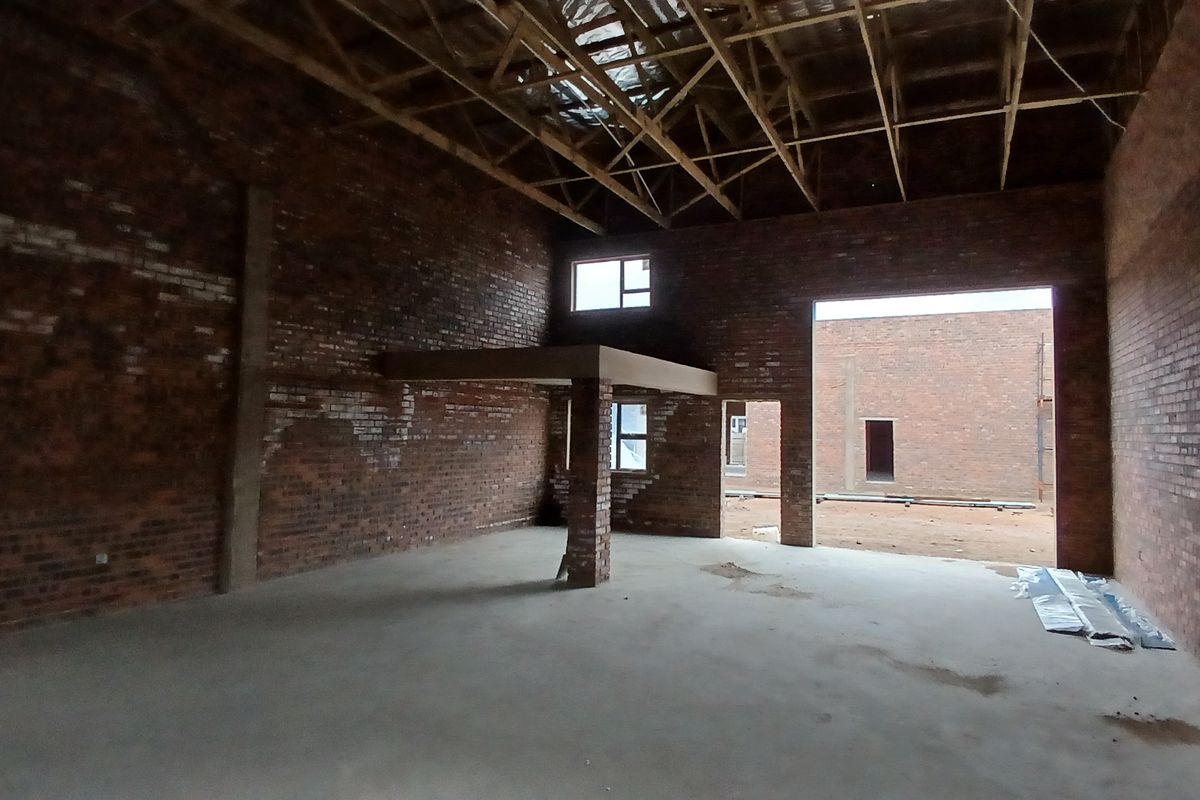 Spacious industrial utility area featuring exposed brick walls, high timber roof trusses, and a mezzanine level, currently in an unfinished construction state.