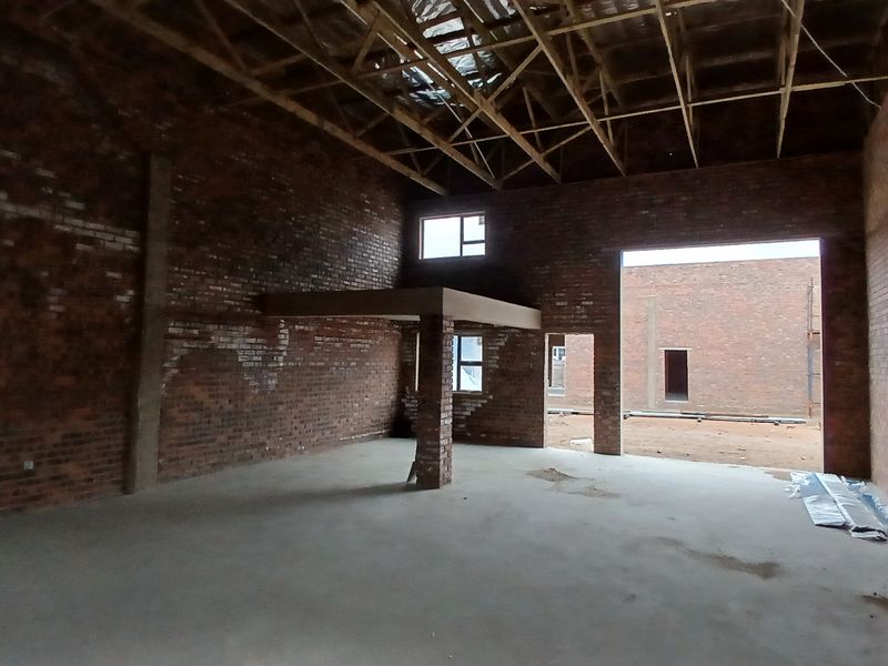Spacious industrial utility area featuring exposed brick walls, high timber roof trusses, and a mezzanine level, currently in an unfinished construction state.