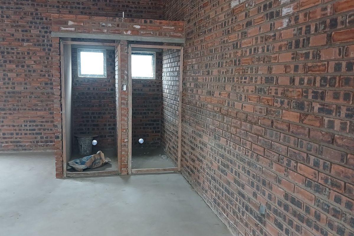 An unfinished industrial bathroom space featuring exposed brick walls, concrete flooring, and plumbing rough-ins, ready for final fit-out and installation of sanitary fixtures.