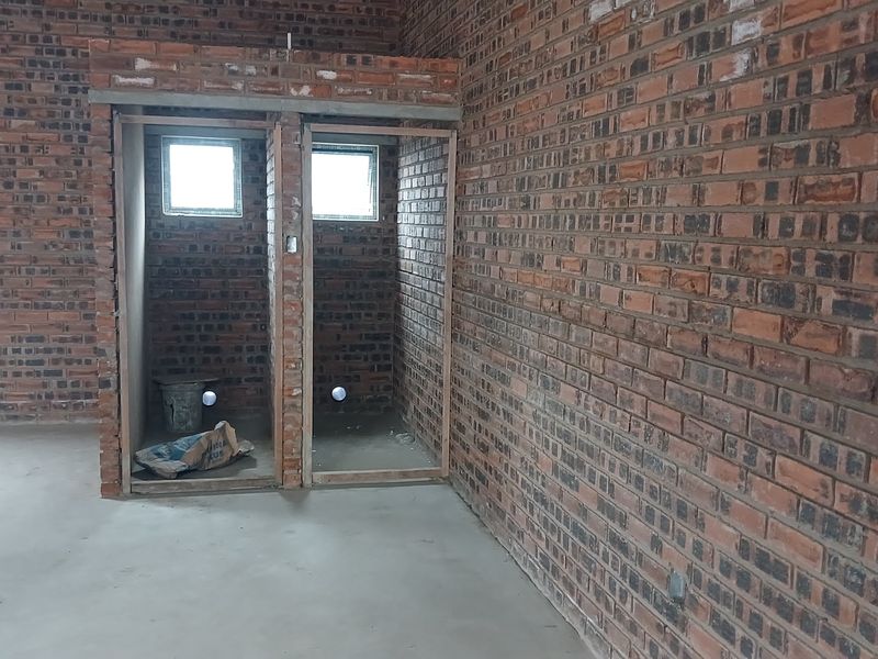 An unfinished industrial bathroom space featuring exposed brick walls, concrete flooring, and plumbing rough-ins, ready for final fit-out and installation of sanitary fixtures.