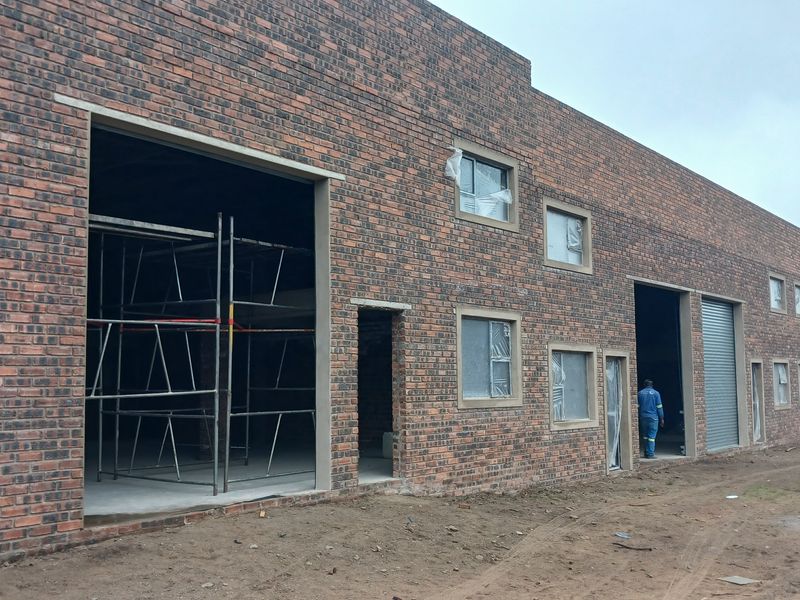 Exterior view of an industrial warehouse building under construction, featuring face brick facade, large entrance bays, and roller shutter doors.