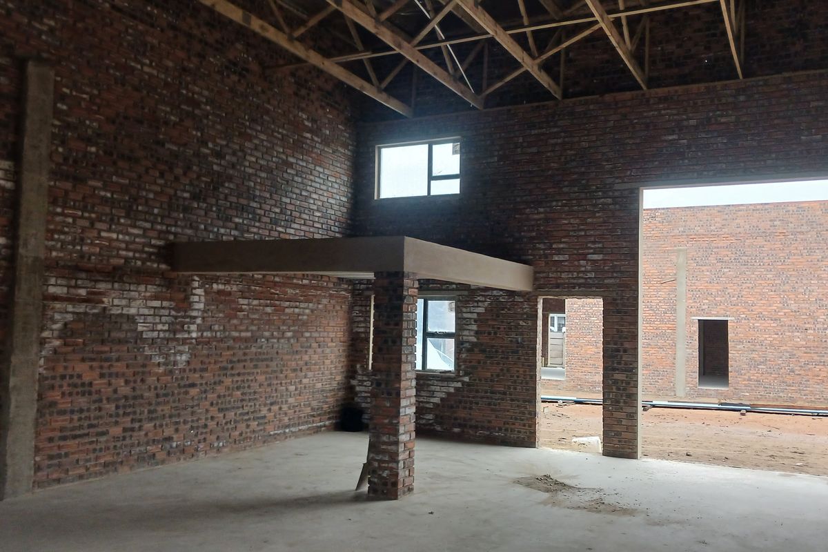 An unfinished industrial space featuring exposed brick walls, high timber roof trusses, and a mezzanine level, offering a versatile blank canvas for development.