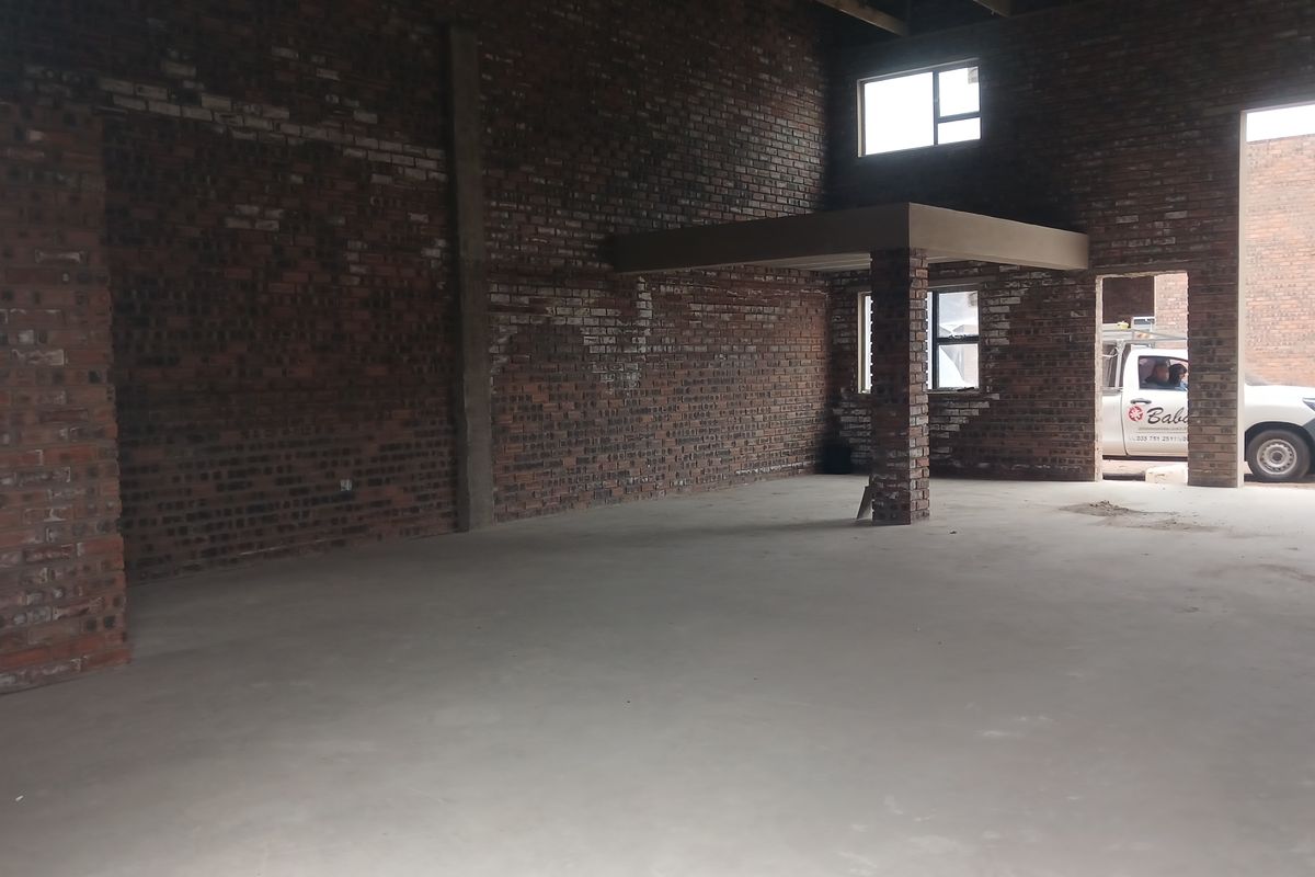 Spacious industrial utility area featuring exposed brick walls, concrete flooring, and a mezzanine level, suitable for workshop or storage use.