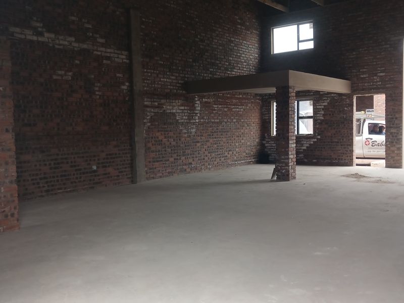 Spacious industrial utility area featuring exposed brick walls, concrete flooring, and a mezzanine level, suitable for workshop or storage use.