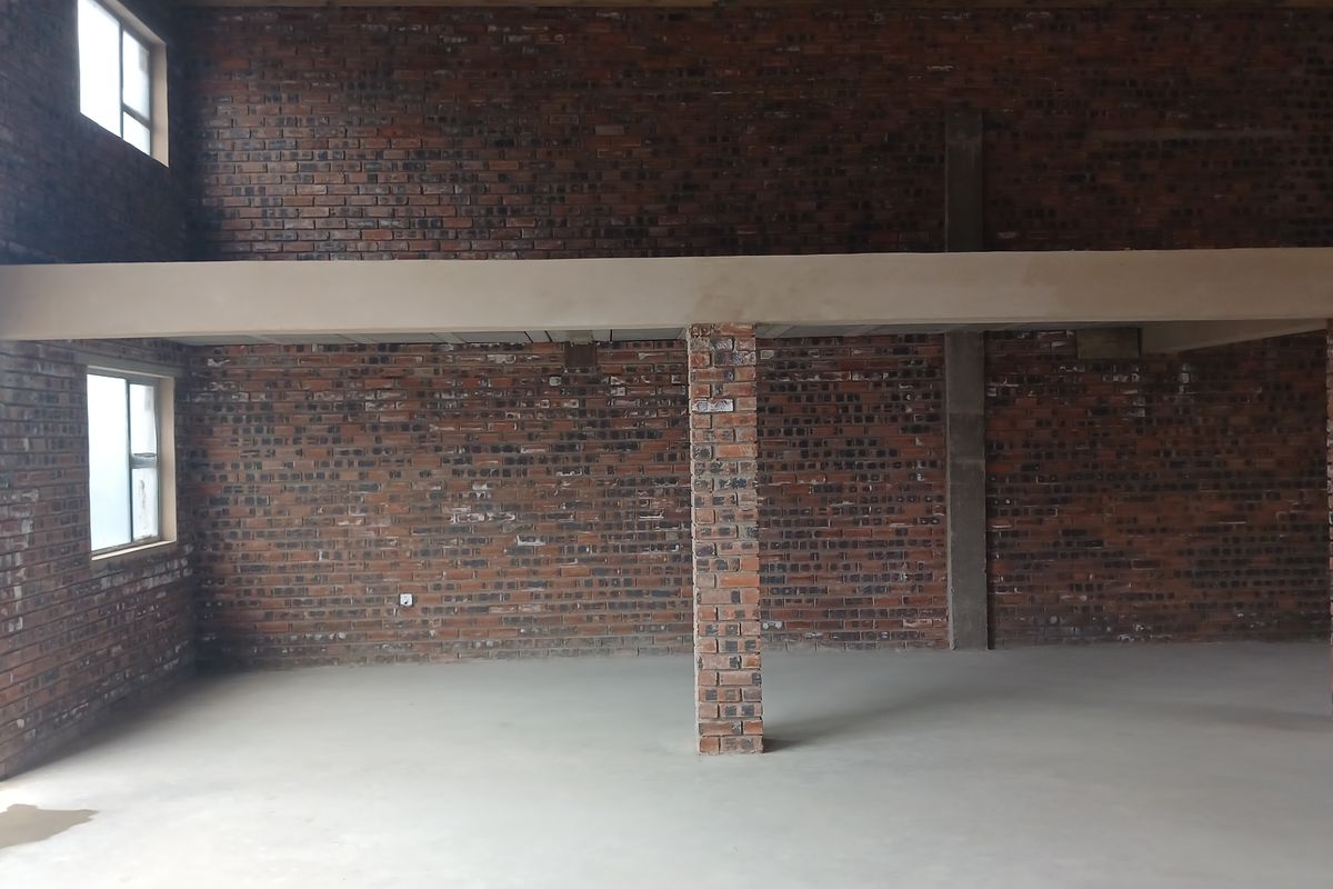 Spacious industrial open-plan area featuring exposed brick walls, concrete flooring, and a mezzanine level supported by brick columns, offering versatile potential for development.