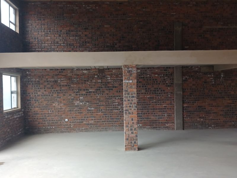 Spacious industrial open-plan area featuring exposed brick walls, concrete flooring, and a mezzanine level supported by brick columns, offering versatile potential for development.