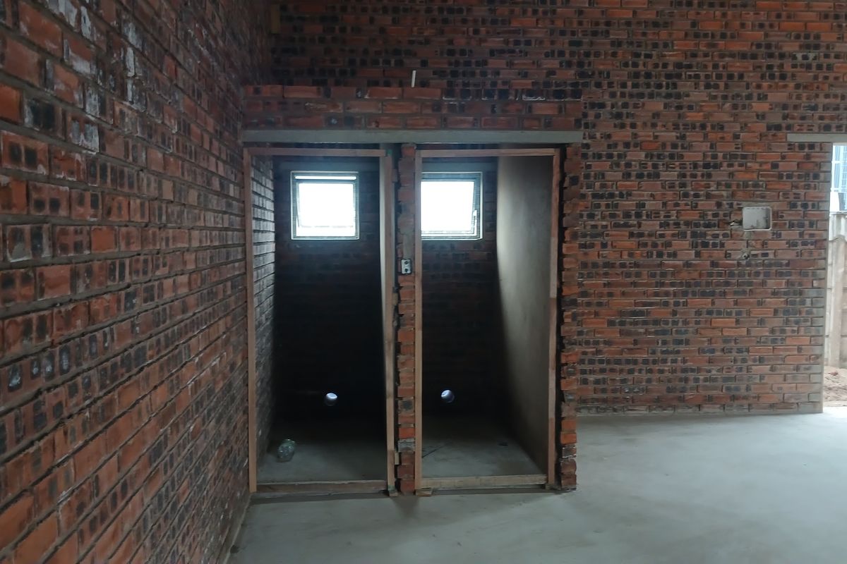 An unfinished industrial utility space featuring exposed brick walls, concrete flooring, and plumbing rough-ins for two separate cubicles.