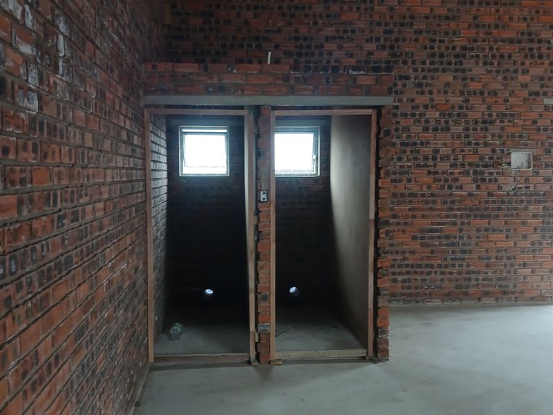 An unfinished industrial utility space featuring exposed brick walls, concrete flooring, and plumbing rough-ins for two separate cubicles.