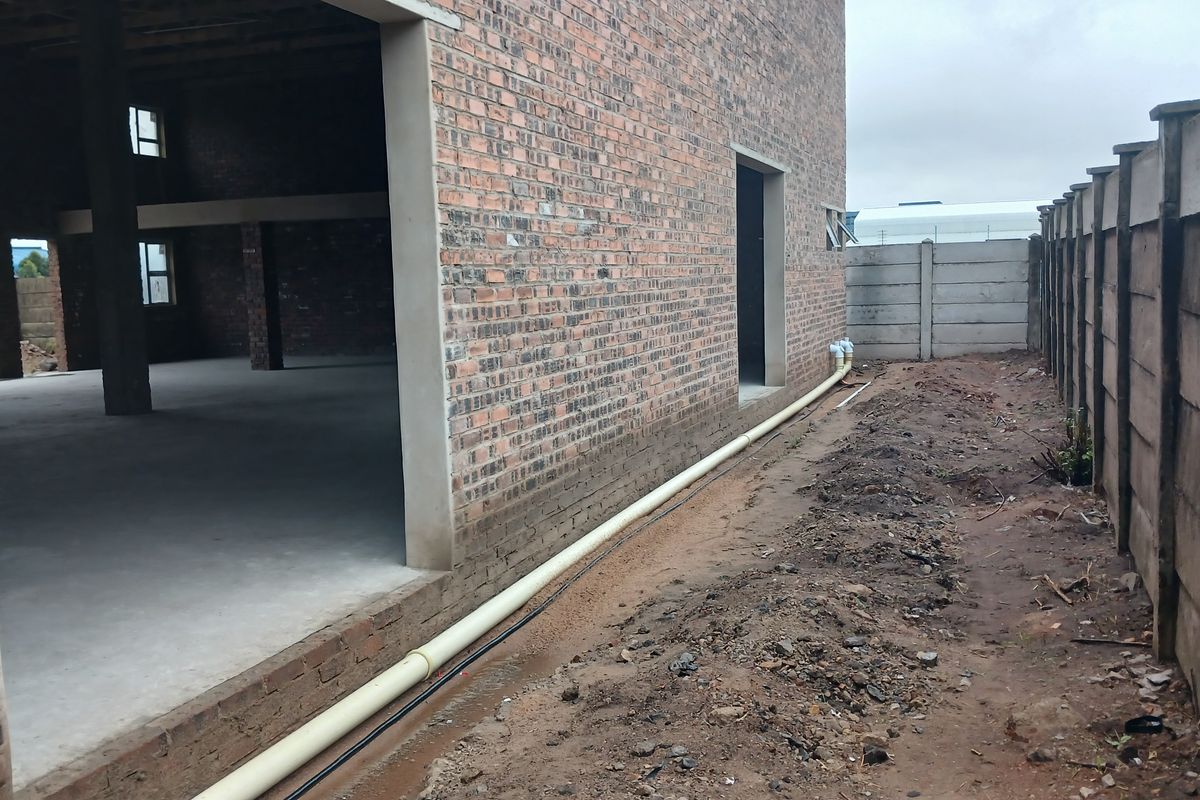 Rear view of an industrial property under construction, featuring exposed brickwork, concrete flooring, and a precast boundary wall with external drainage infrastructure.