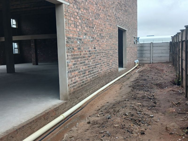 Rear view of an industrial property under construction, featuring exposed brickwork, concrete flooring, and a precast boundary wall with external drainage infrastructure.
