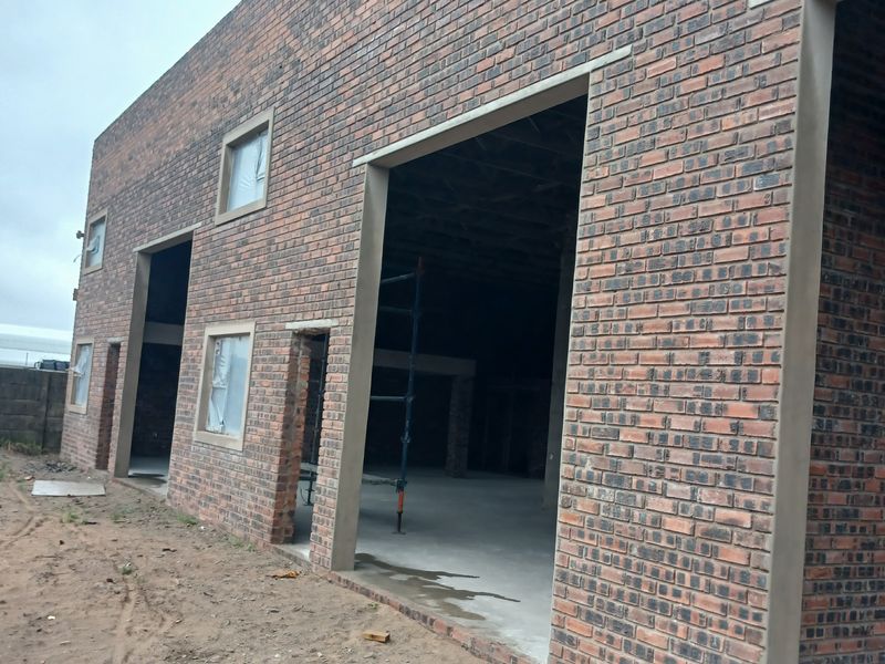 Exterior view of an industrial building under construction, featuring face brick facade, large open bays, and unfinished surrounding grounds.