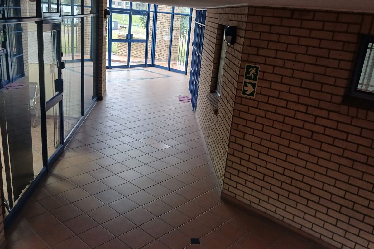 A clean, industrial-style hallway featuring exposed brick walls, tiled flooring, and extensive aluminium-framed glass partitioning for natural light.
