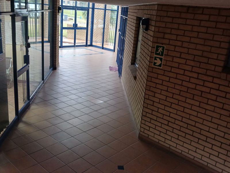A clean, industrial-style hallway featuring exposed brick walls, tiled flooring, and extensive aluminium-framed glass partitioning for natural light.