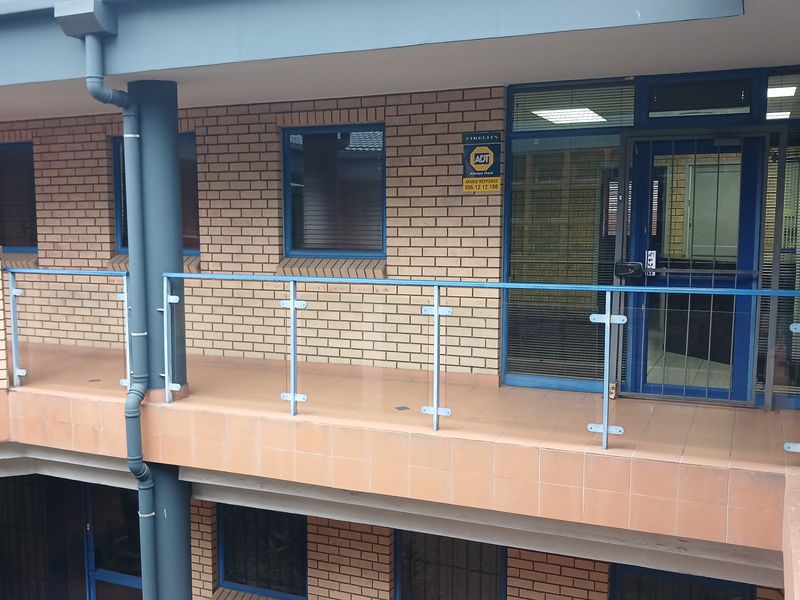 Exterior view of an industrial office building featuring a brick facade, tiled balcony with a glass balustrade, and secure aluminium-framed entrance.