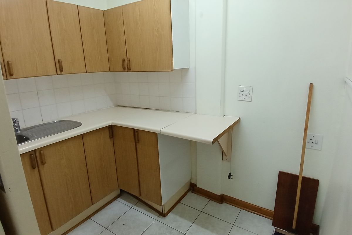 A compact kitchen area featuring wood-look laminate cabinetry, a stainless steel sink, tiled backsplash, and ceramic floor tiles.