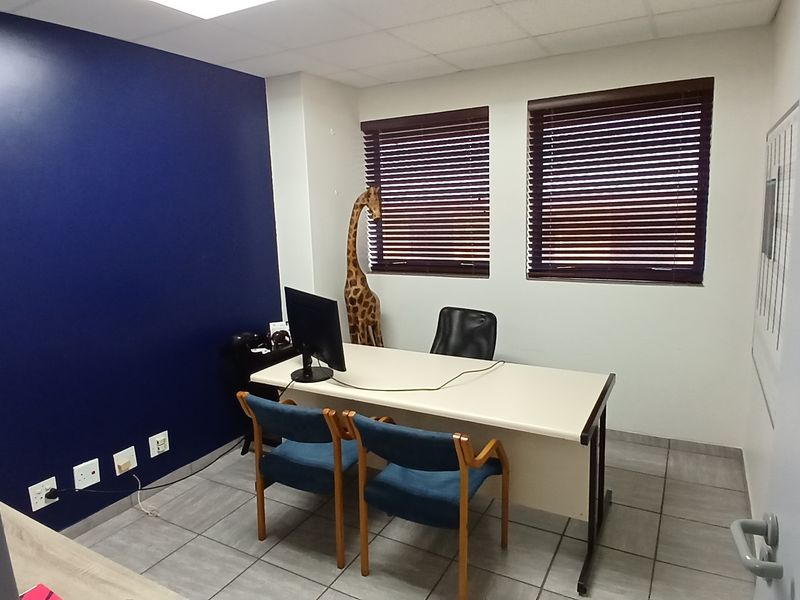A functional office space featuring tiled flooring, a drop ceiling, and dual windows with venetian blinds.