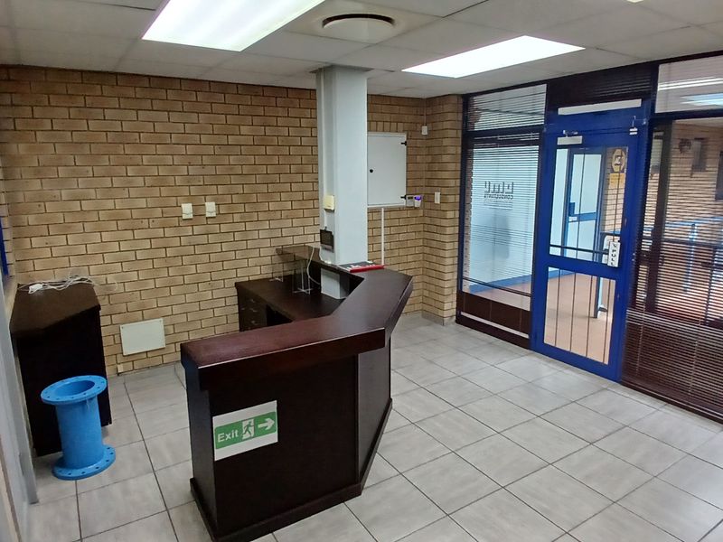A functional industrial office entry area featuring exposed brick walls, tiled flooring, a drop ceiling, and a built-in reception desk.