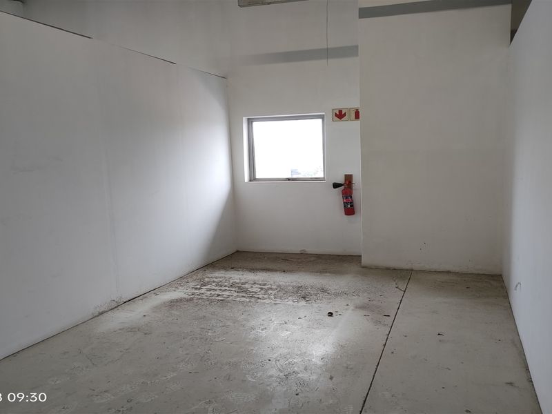 An empty industrial utility space featuring concrete flooring, a fire extinguisher, and emergency signage, suitable for storage or workshop use.