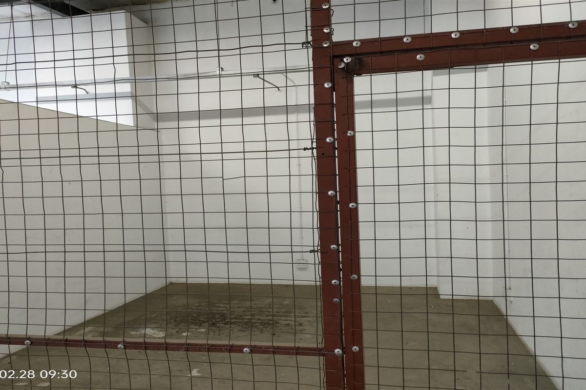 A secure, enclosed utility or storage area featuring concrete flooring and a heavy-duty wire mesh partition.