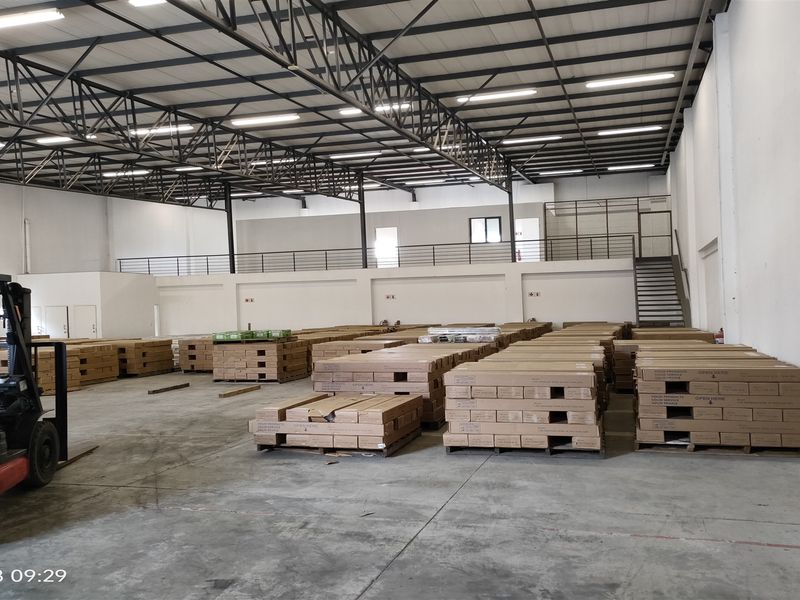Spacious industrial warehouse featuring high ceilings with exposed steel trusses, a mezzanine level with staircase access, and durable concrete flooring.