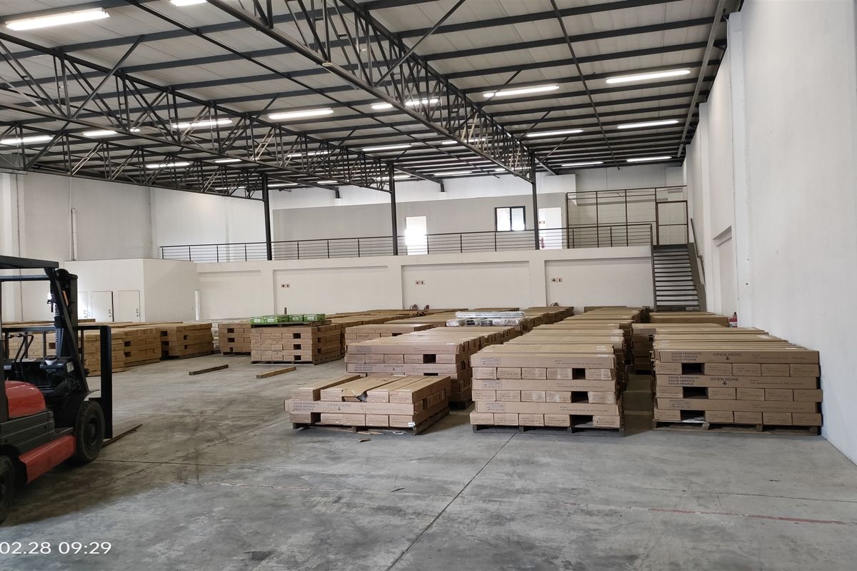 Spacious industrial warehouse featuring high ceilings with exposed steel trusses, a mezzanine level with staircase access, and durable concrete flooring.
