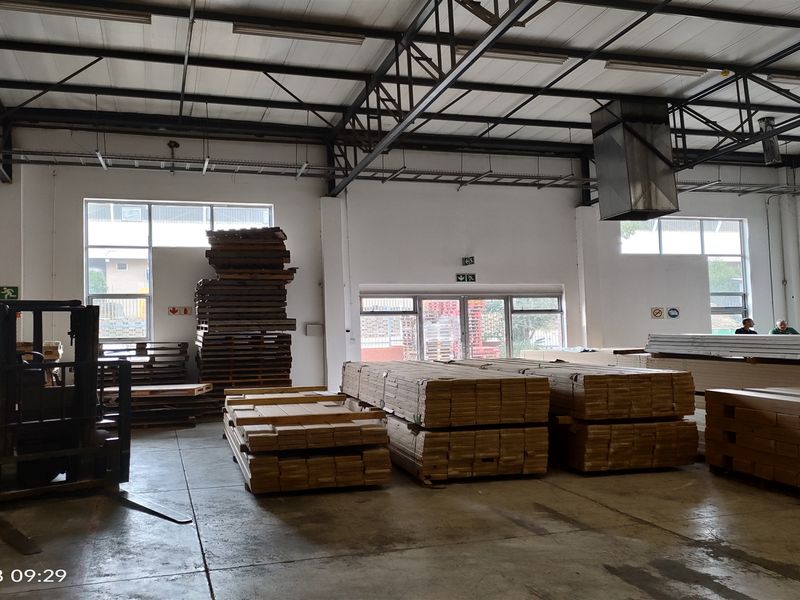 Spacious industrial warehouse unit featuring high ceilings with exposed steel trusses, concrete flooring, and a large roller shutter door for easy access.