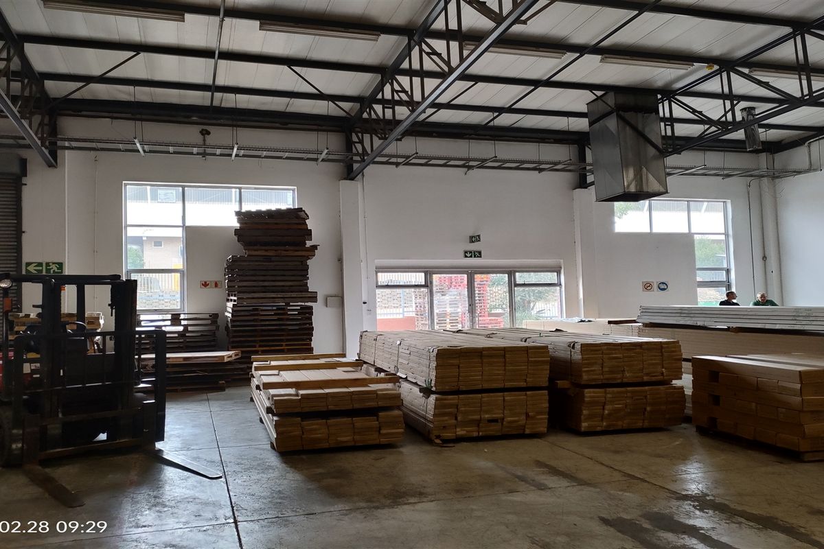 Spacious industrial warehouse unit featuring high ceilings with exposed steel trusses, concrete flooring, and a large roller shutter door for easy access.