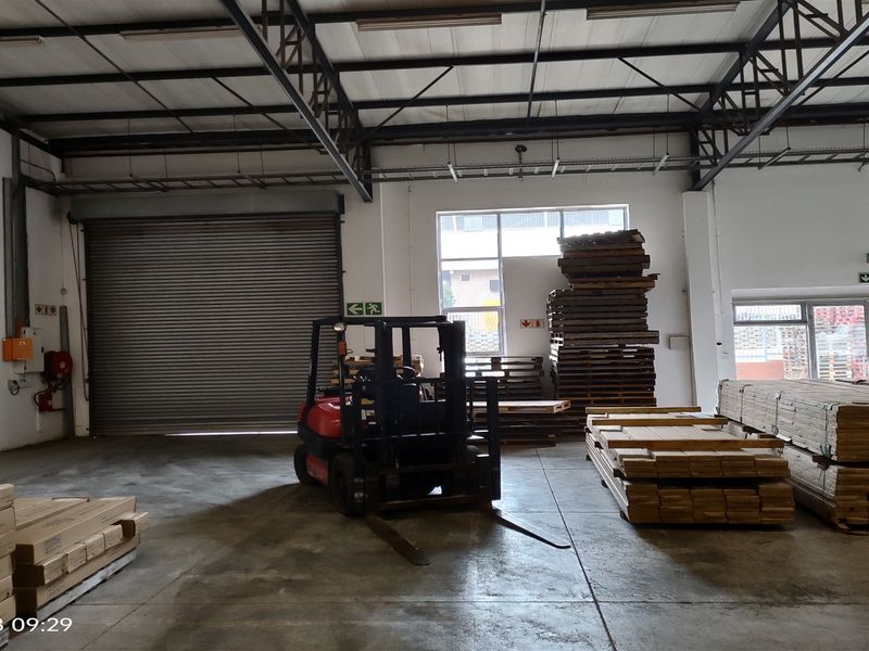 Spacious industrial warehouse unit featuring high ceilings with exposed steel trusses, concrete flooring, and a large roller shutter door for easy access.