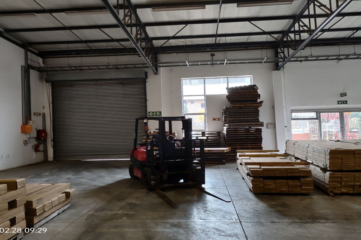 Spacious industrial warehouse unit featuring high ceilings with exposed steel trusses, concrete flooring, and a large roller shutter door for easy access.