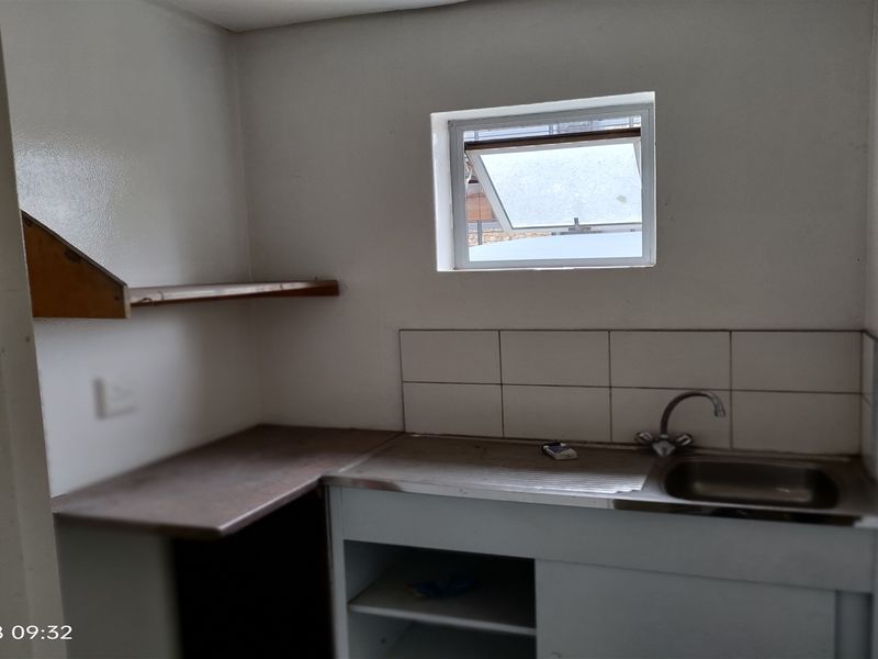 A functional scullery or utility area featuring a stainless steel sink, tiled splashback, and open shelving, suitable for renovation or modernization.