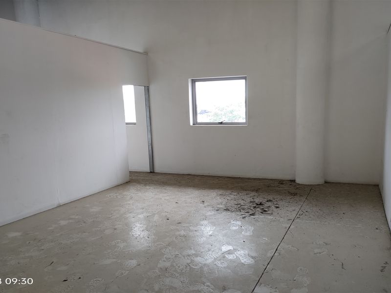 An empty industrial utility space featuring concrete flooring, a structural column, and a single window, suitable for various commercial or storage applications.