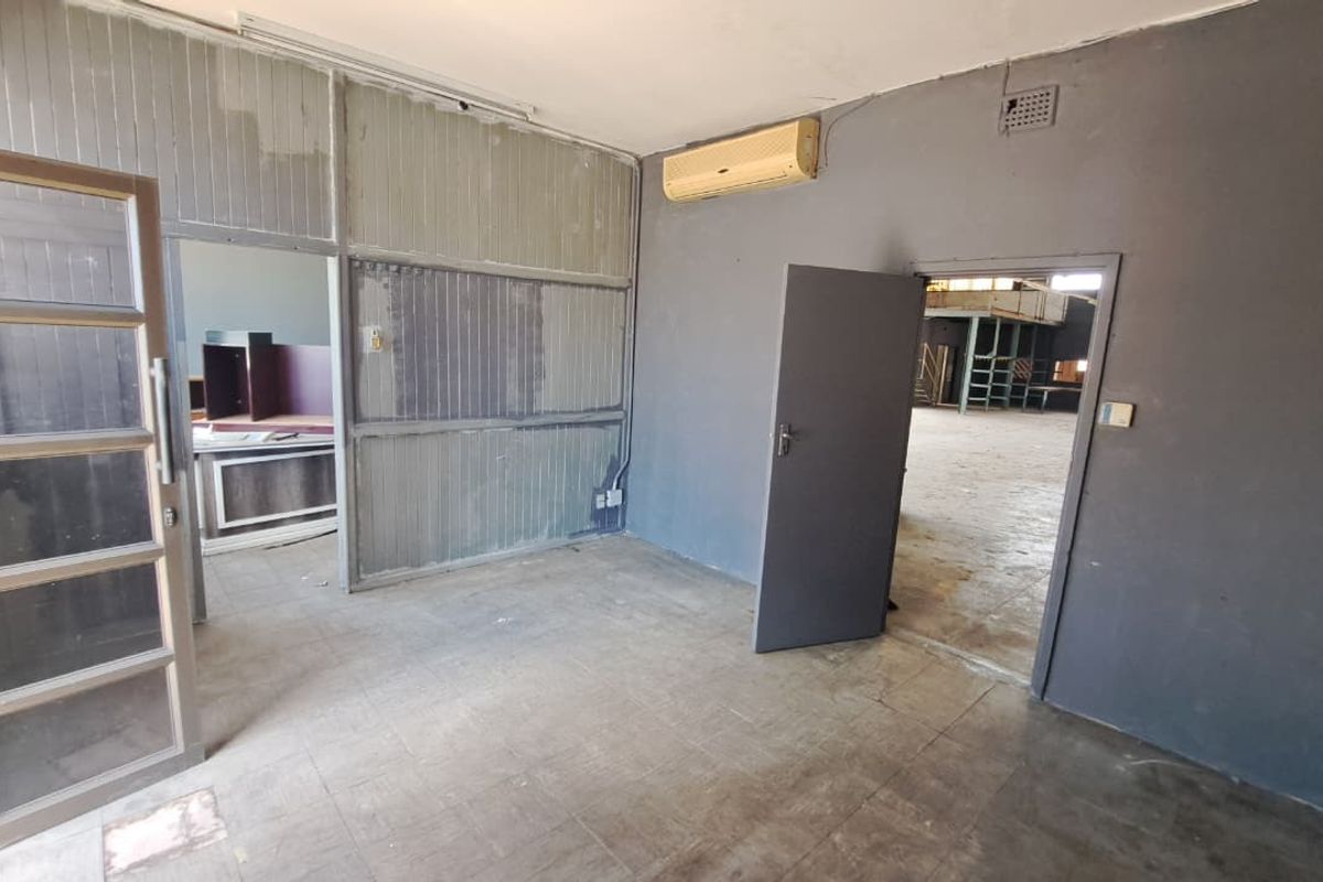 An empty office space featuring tiled flooring, a partition wall, and an integrated air conditioning unit, showing signs of wear and tear.