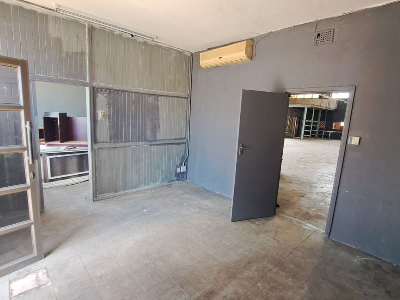 An empty office space featuring tiled flooring, a partition wall, and an integrated air conditioning unit, showing signs of wear and tear.