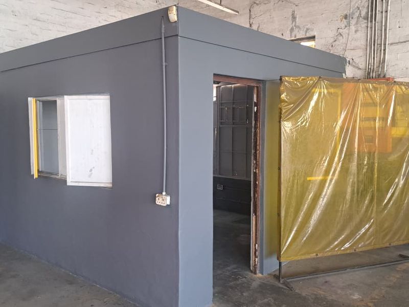 A functional utility office or partitioned workspace within an industrial setting, featuring painted brick walls and basic electrical infrastructure.