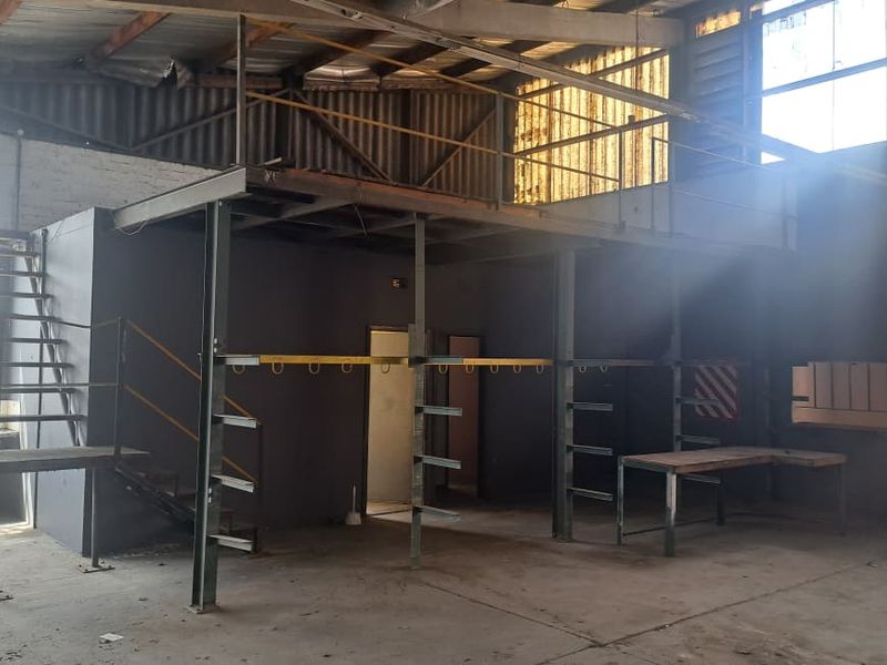 Industrial utility space featuring a steel mezzanine level, staircase, and concrete flooring, suitable for workshop or storage use.