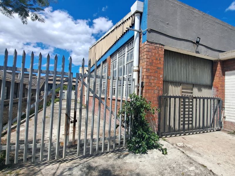 Rear exterior view of an industrial property featuring brick construction, steel-framed windows, a roller shutter door, and perimeter security fencing.