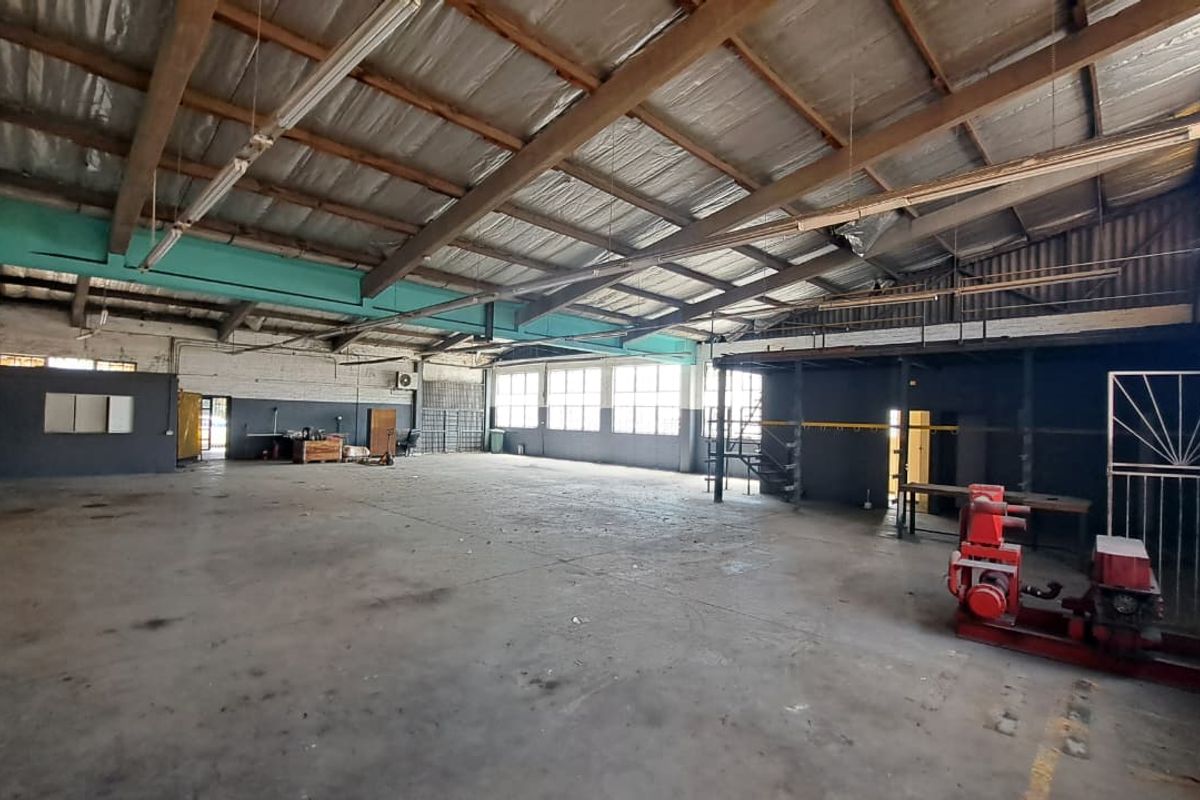 Spacious industrial warehouse featuring exposed timber roof trusses, concrete flooring, large windows for natural light, and a mezzanine level for additional storage or office space.