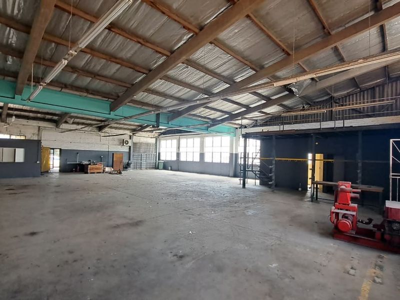 Spacious industrial warehouse featuring exposed timber roof trusses, concrete flooring, large windows for natural light, and a mezzanine level for additional storage or office space.